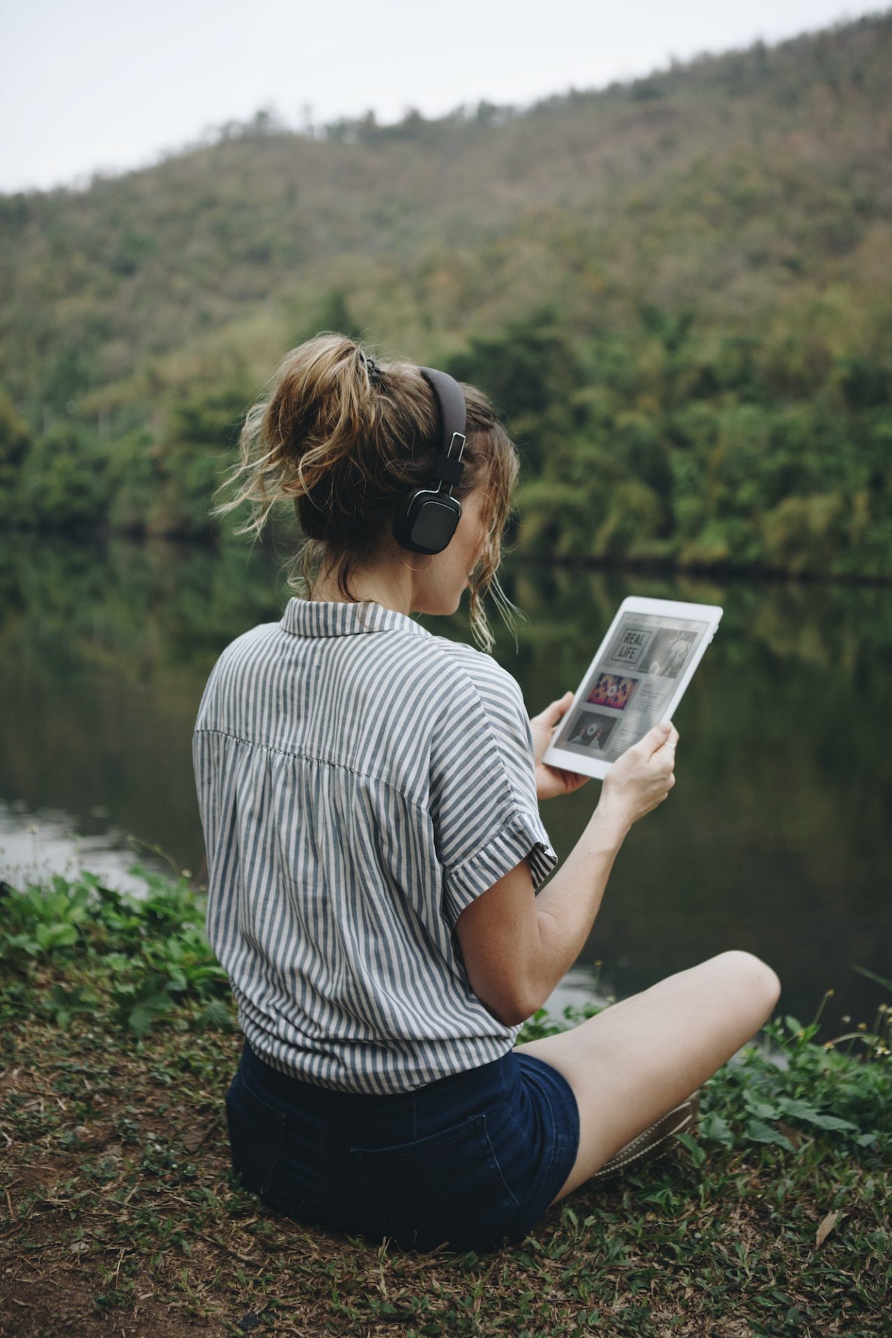 Woman alone in nature listening to music with headphones and digital tablet