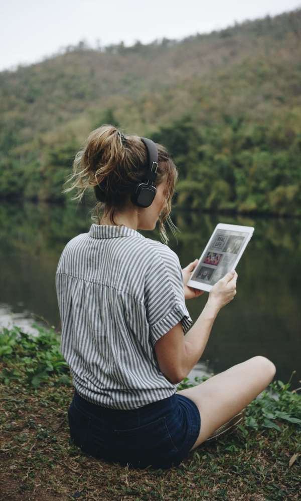 Woman alone in nature listening to music with headphones and digital tablet